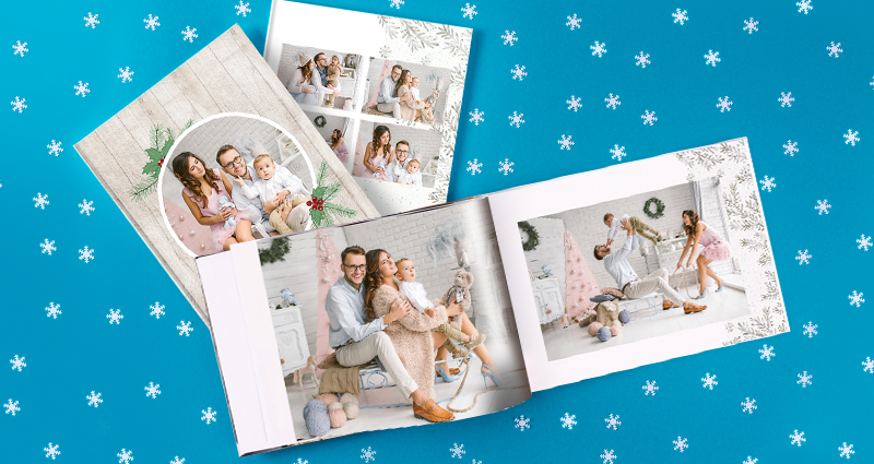 3 vianočné fotoknihy s rodinnými fotografiami - dve uzavreté, jedna (horizontálna) otvorená. Okolo snehové vločky na modrom pozadí.
