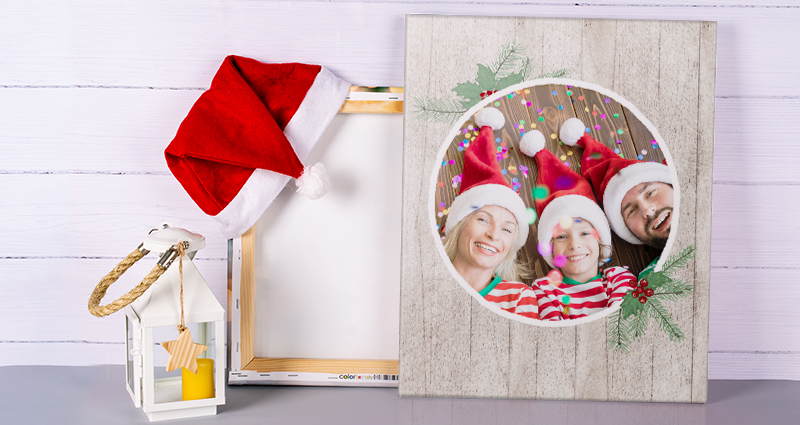 Une toile photo de Noël , derrière une toile photo inversée avec un bonnet de Père Noël. Une lanterne blanche à côté. Au fond un mur de planches.