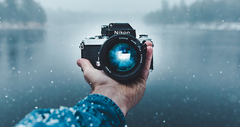 Foto di una macchina fotografica su una mano protesa verso un lago