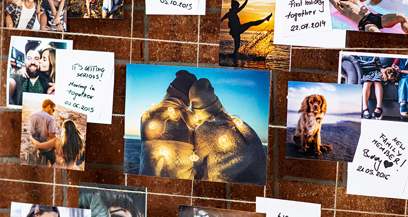 A close-up on the photos of the newly-weds presenting different stages of their relationship, with captions. The photos are attached to a hemp string. A red brick wall in the background