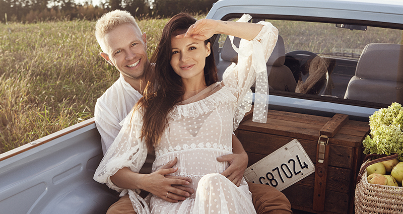 A couple during a pregnancy photo shoot in a car on a meadow 