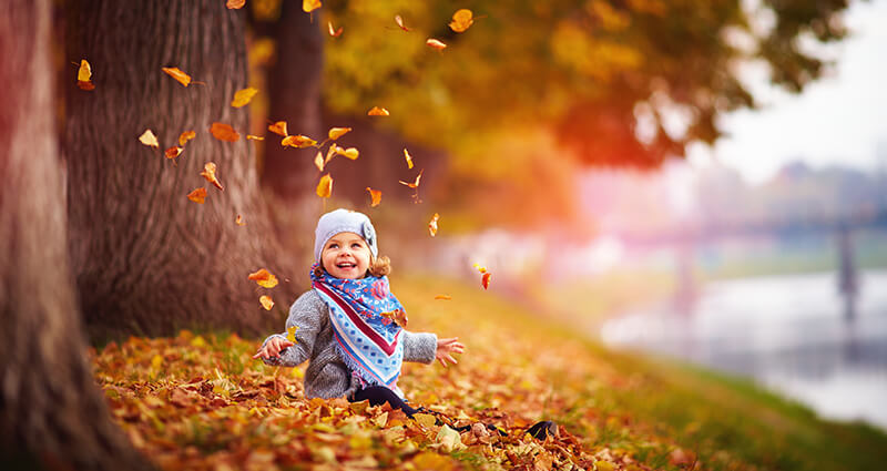 Ein kleines Mädchen spielt inmitten der Blätter im Park