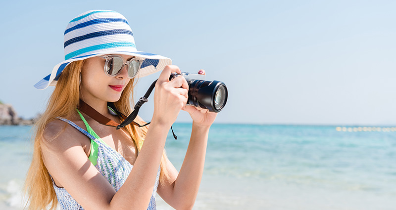 Una ragazza con un cappello e una fotocamera sulla spiaggia.