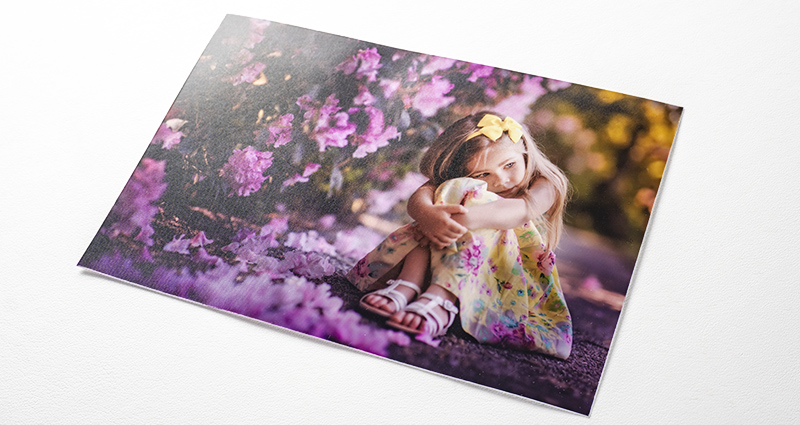 A photo of a girl sitting next to purple flower bushes – a photo printed on the PREMIUM SILK paper.