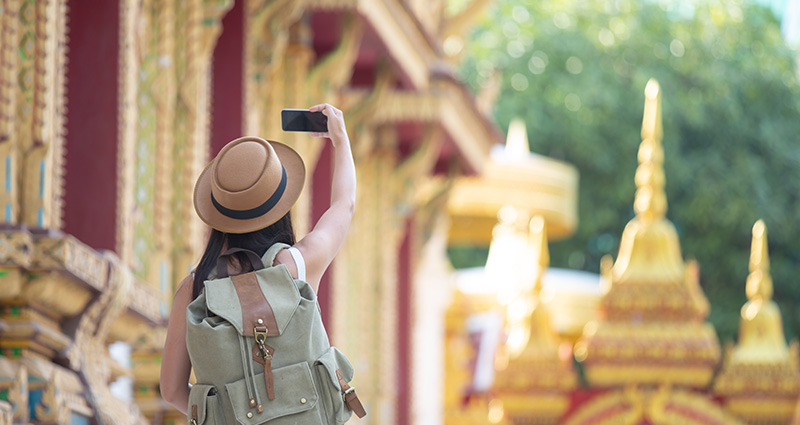 Turisttė su kuprine atostogose Azijoje, fotografuojanti naudojant fotoaparatą išmaniajame telefone