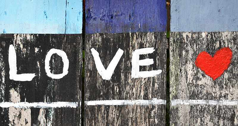A word LOVE written with white paint on black and grey wooden planks, a red heard next to it; planks painted with blue paint in the upper part