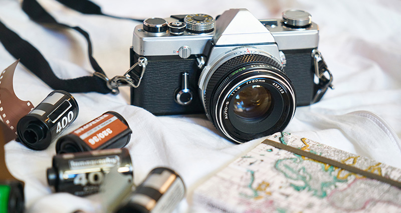Een analoge camera geplaatst naast rolletjes en een notitieblok met reistips