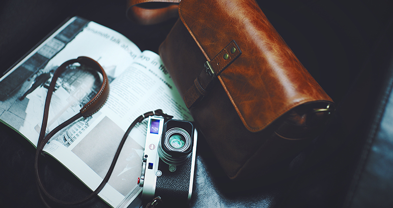 Una bolsa de cuero marrón, un periódico y una cámara sobre un sillón negro.