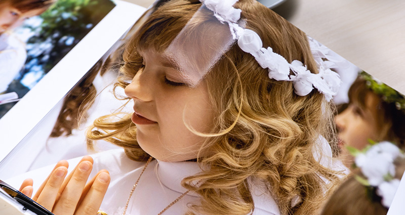 Le zoom sur une photo d’une fille aux cheveux blonds pendant la Première Communion, photo imprimée dans un starbook.