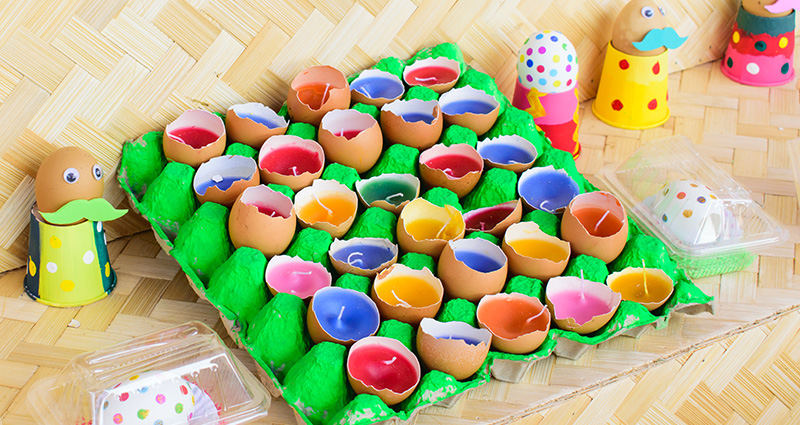 Colourful candles made from blown eggs in a green egg carton.