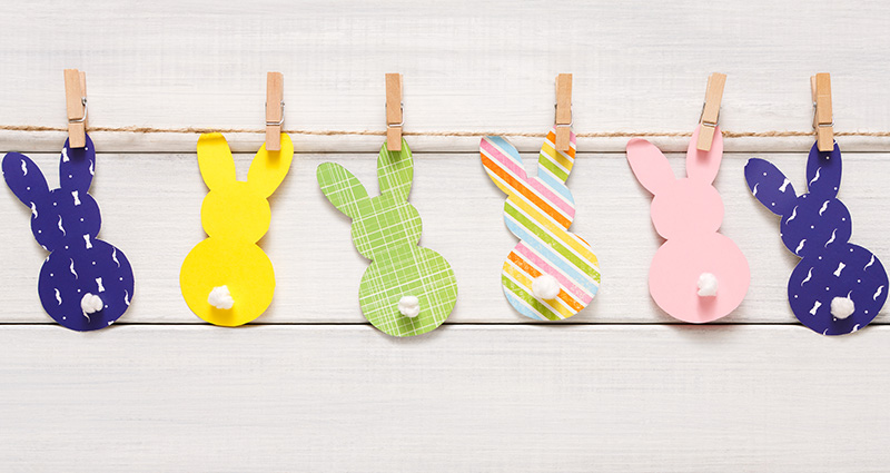 Colourful paper bunnies attached by wooden clothespins to a jute twine hanging close to the wall.