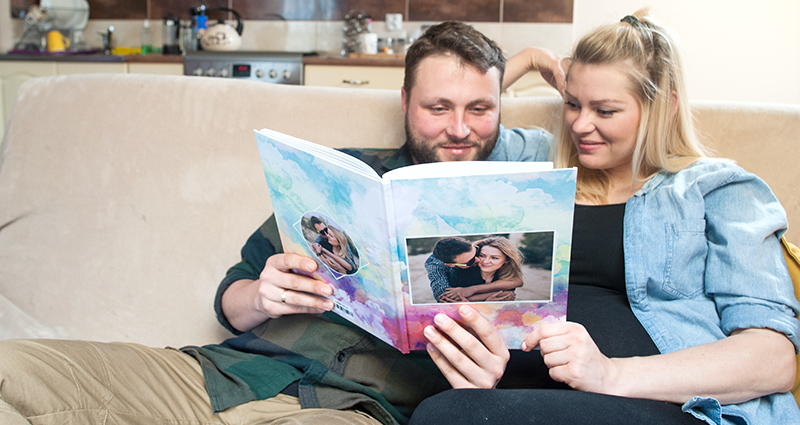 Couple sitting on the couch and reading a wedding guest bookPareja en un sofá mirando sus libro de firmas. 