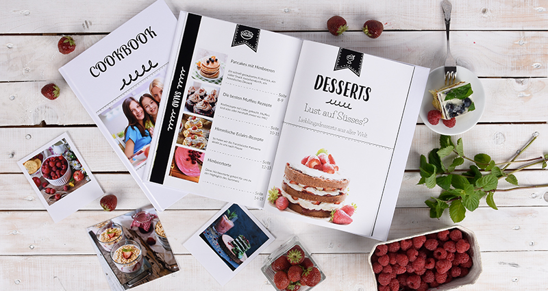 Ein Kochbuch mit Nachtisch-Rezepten, Insta und Retro Fotoabzüge, Himbeeren, Minz und ein Kuchen auf dem Teller