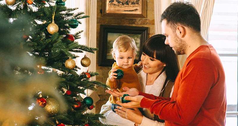 Una familia de tres personas decorando un árbol navideño.