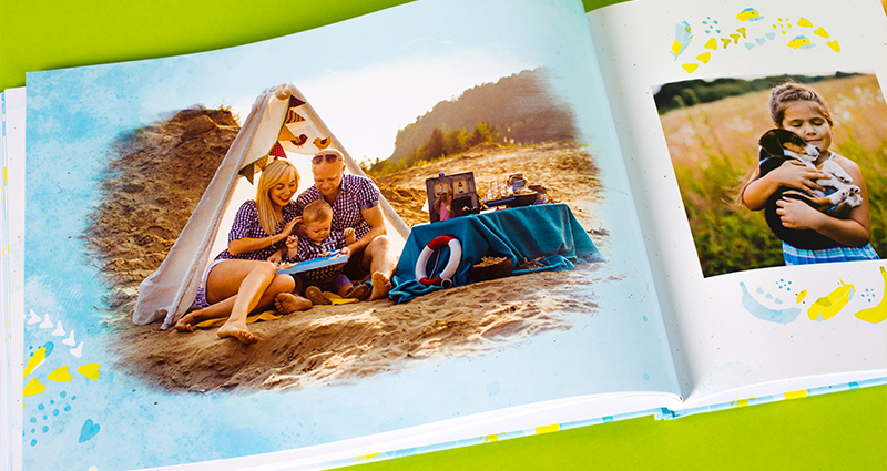 Eine Nahaufnahme auf ein Bild von einer Familie im Zelt; das Bild ist in einem Fotobuch aufgedruckt und mit einem Rahmen und einigen Cliparts geschmückt