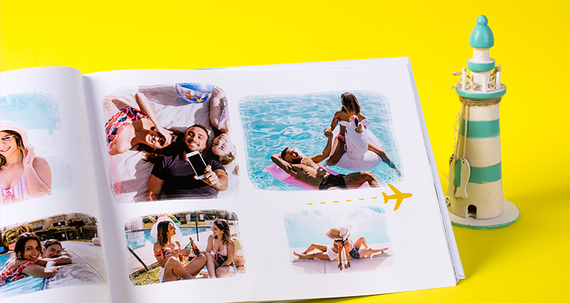 Focus on a page of a holiday photobook with pictures of friends lying next to a ceramic figurine presenting a lighthouse 