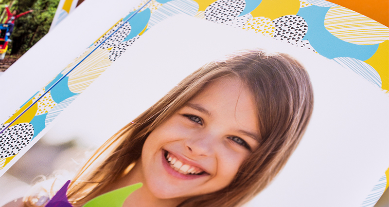 Le zoom sur la photo qui présent le visage d’une fille souriante tenant dans les mains un moulin à vent coloré- photo imprimée dans un livre photo 7C.