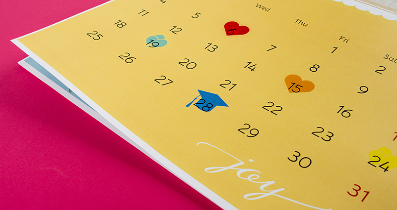 Detailní záběr na kalendárium kalendáře s označenými svátky, růžové pozadí.
