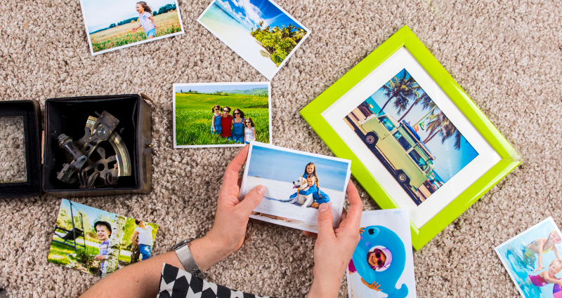 Zoom na dlane osoby pozerajúcej si fotografie z dovolenky rozložené na koberci. 