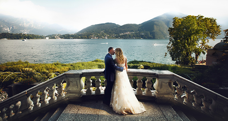 La foto di una coppia di sposi sulle scale con vista; sullo sfondo il lago di Come e i monti.