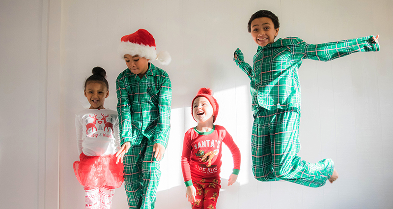 Four jumping kids wearing Christmas pyjamas, a white wall in the background
