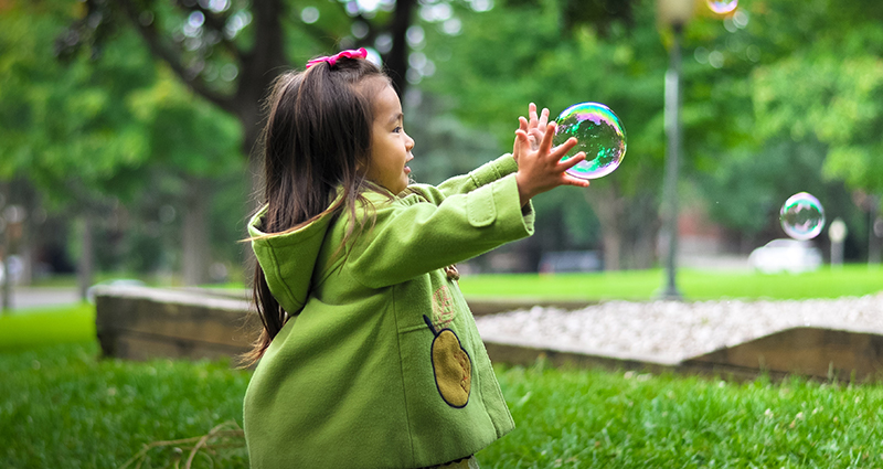Mažoji mergaitė parke gaudo muilo burbuliukus.
