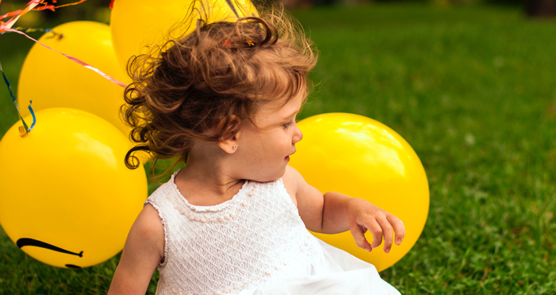 Bambina con un abito bianco con palloncini gialli nel parco