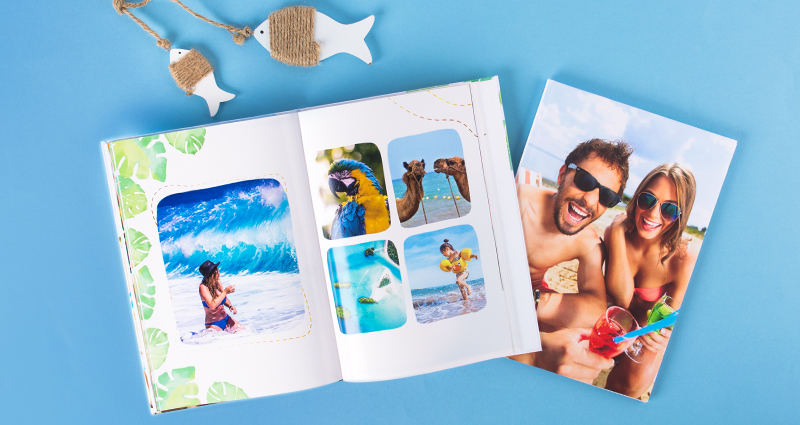 Holiday photobooks – one of them with a photo collage is open, the closed one’s cover presents a photo of a couple, two wooden fish above them. 