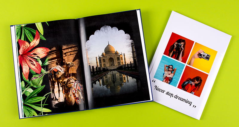 Fotobuch vom Sommerurlaub, ein Fotobuch ist geöffnet und zeigt die Bilder von einer großen, exotischen Blume und von Taj Mahal, das zweite Fotobuch ist geschlossen und hat ein Cover mit einer Foto-Collage aus 4 bunten Bildern und mit einer Aufschrift Never stop dreaming 