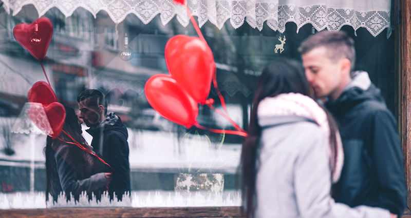 Kissing couple holding red heart-shaped balloons