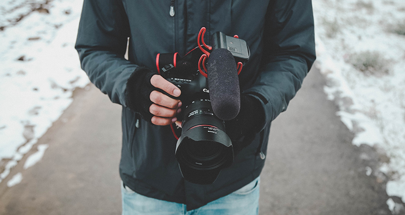 Man holding a camera in hands in fingerless gloves; focus on his body