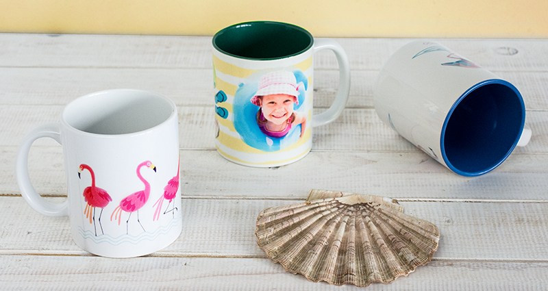 Photo mugs on the desk – one mug with a photo, two mugs with a pre-made template lying next to a seashell. Fototazas sobre la mesa – una taza con foto, dos tazas creadas de las plantillas prediseñadas, una concha de mar al lado.