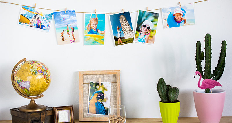 Photo of holiday prints hanging on a string and pinned with wooden clips; a globe put on a retro box on the left, two cactuses in coloured flowerpots on the right.