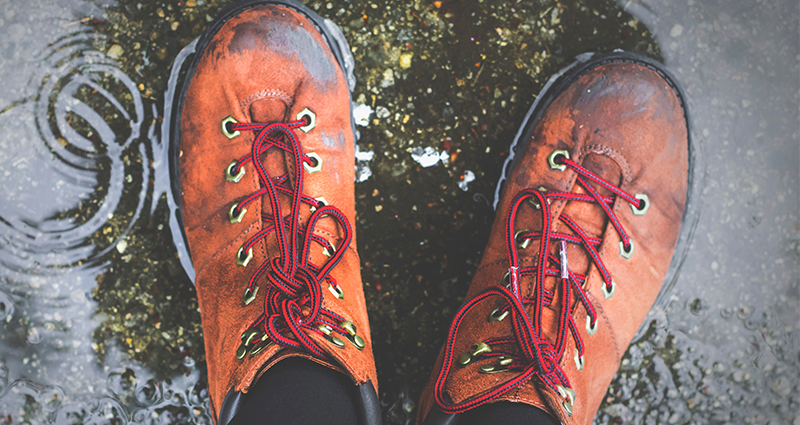 Foto de los pies en zapatos de color naranja, reflejo de una corona de árbol en un charco. 