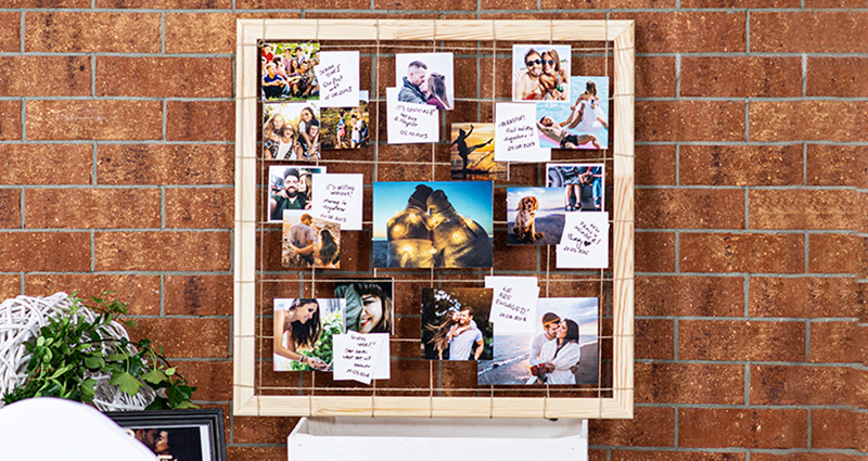 Photos of the newly-weds, showing their love story, attached to a hemp string tied to a wooden frame, captions placed next to the photos. The frame stands on a white box, a red brick wall in the background