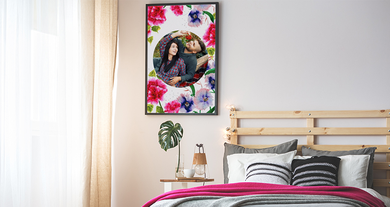 Foto di una camera da letto con decorazioni rosa-grigie e un'enorme finestra luminosa. Accanto al letto una grande tela fotografica con un tema floreale e una foto di una coppia innamorata.