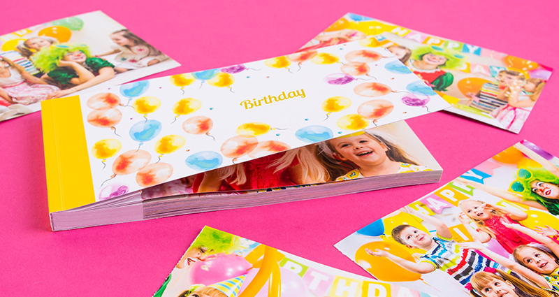 Un sharebook avec la couverture soulevée Balons Colorés, autour des photos detachées d’une fête anniversaire,