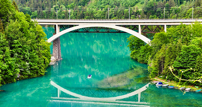 Tall bridge in the forest reflected in a turquoise water surface