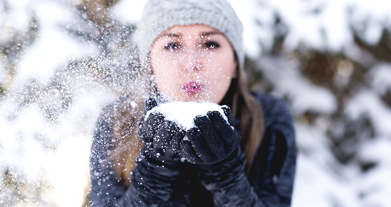 Foto von Teddy Kelley von Unsplash - eine Frau mit der Mütze bläst eine Handvoll Schnee im Winterwald