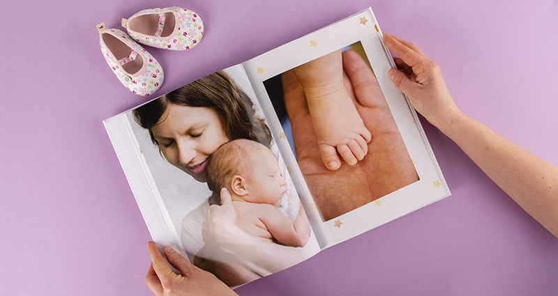 Frau hält in der Hand ein Fotobuch mit Bildern vom Baby-Fotoshooting. Oben die Babyschuhe.  