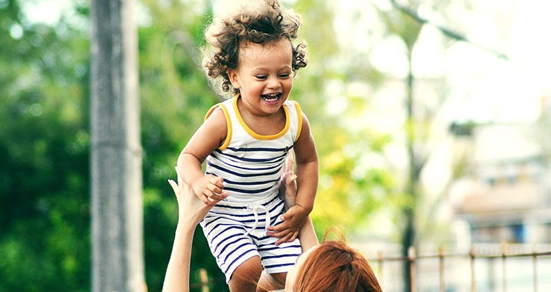 Mujer levantando a un niño sonriente.