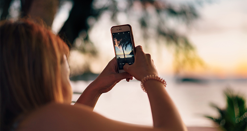 Žena fotografující palmu při západu slunce.
