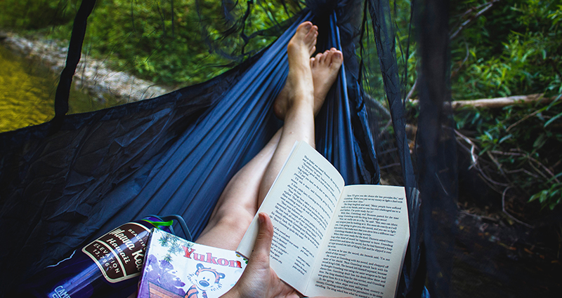 Las piernas de una mujer que lee un libro en una hamaca con mosquitero en la selva. 