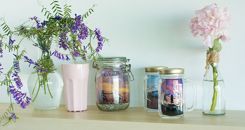 Une composition de photos placées dans des pots en verre et mises sur une étagère.