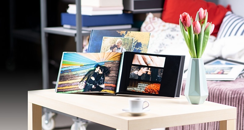 2 starbooks, with pictures of a couple, on a bright table and tulips in a vase next to them. A couch in the background and photo products on the shelves.