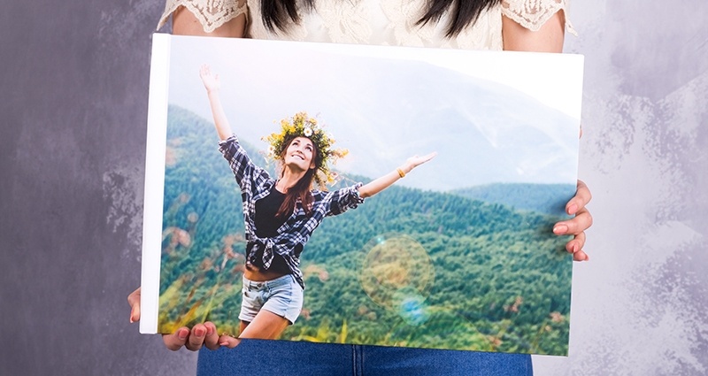 A woman holding a closed photo book A3 Landscape, focus on the cover with a girl wearing a wreath in the mountains