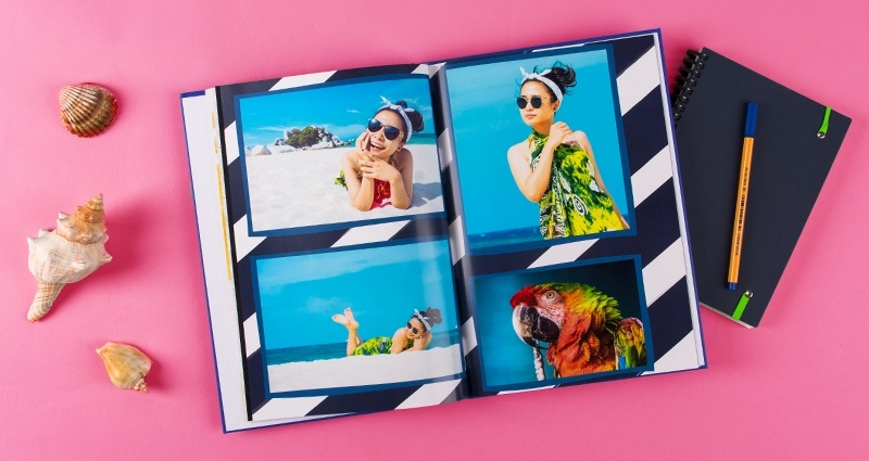 Atostogų Fotoknyga - nuotraukos ant baltai mėlynojo fono su juostelėmis, šalia užrašų knygutės ir jūrų kriauklė