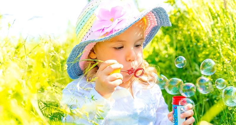 Kleines Mädchen pustet Seifenblasen auf der Wiese 