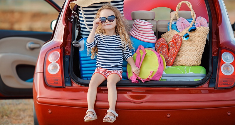 Foto de una niña en un coche lleno de maletas.