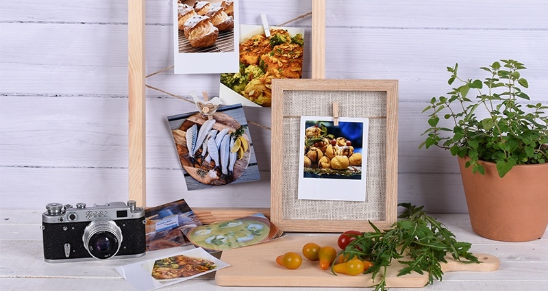Fotos de comida impresas en forma de insta fotos y revelados retro en marcos, junto a una maceta con hierbas, tomates y una cámara.